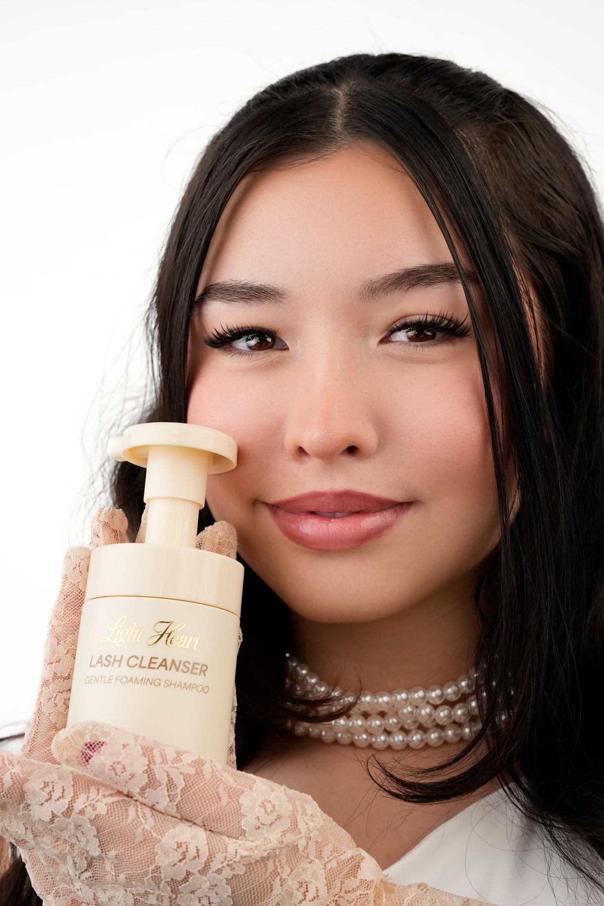 Light Heart Beauty Gentle Foaming Lash Cleanser held by a woman wearing lace gloves and a pearl necklace